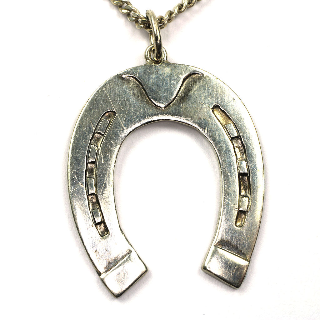 Vedhæng af sølv forestillende hestesko i en halskæde af sølv
